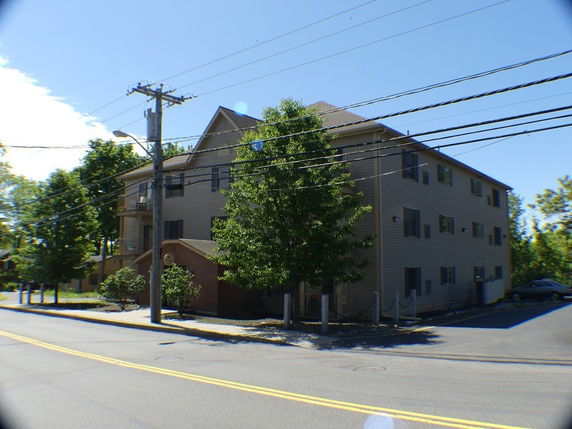 Front view of a multi-story residential building with trees and a parking area.