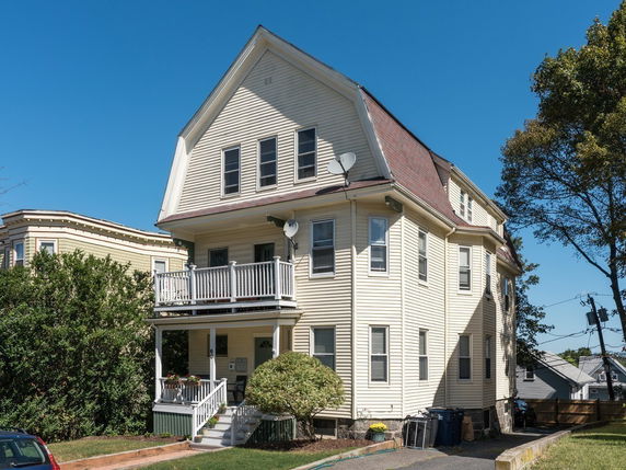 Front view of a multi-story house with beige siding and a gabled roof.