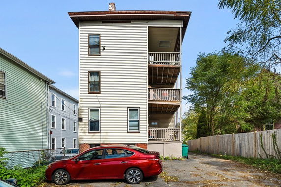 Side view of a multi-story building with balconies and a parked car.