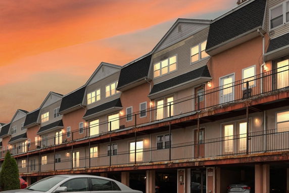 Front view of a multi-story residential building with multiple balconies and a parking area underneath.