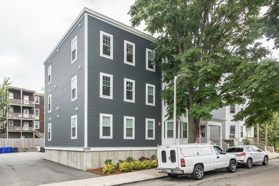 Front view of a multi-story residential building with gray siding and multiple windows.