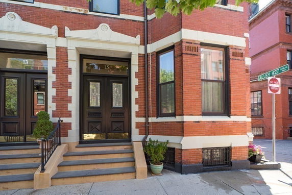 Front view of a brick building entrance with steps and decorative trim.