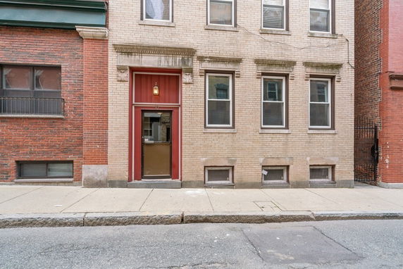 Front view of a three-story brick building with a red entrance door.