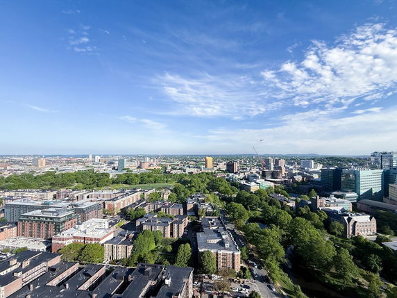 Aerial wide angle view of a cityscape with buildings, roads, and trees under a clear blue sky.