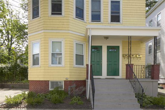 Front view of a two-story house with yellow siding and green doors.