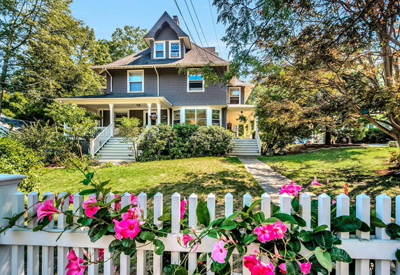 Front view of a multi-story house with a gable roof and wraparound porch.