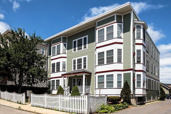 Front view of a three-story residential building with green siding and white trim.