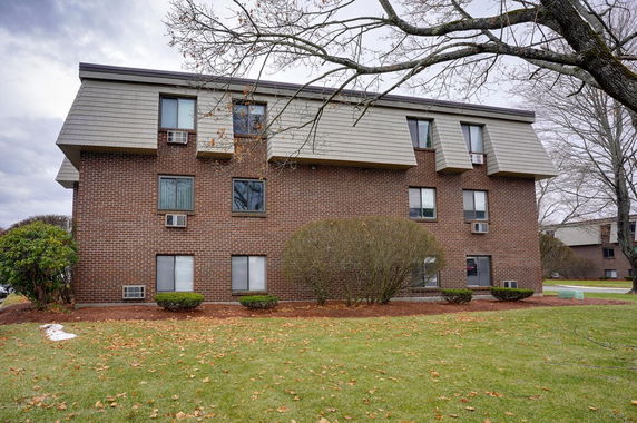 Front view of a multi-story brick apartment building with multiple windows and a sloped roof.