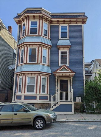 Front view of a three-story blue house with decorative red and white trim.