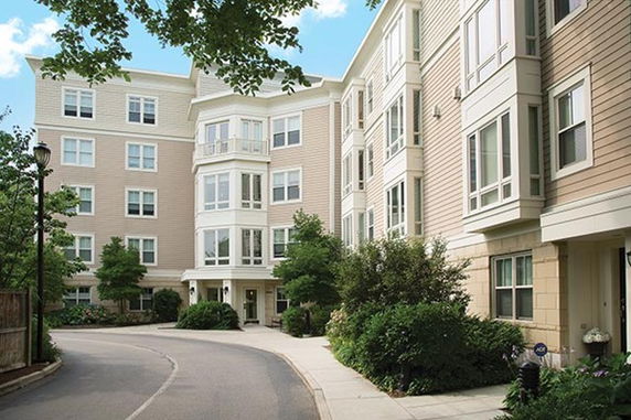 Front view of a multi-story residential building with large windows and a curved driveway.