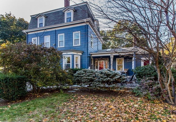 Front view of a three-story blue house with a porch and multiple windows.