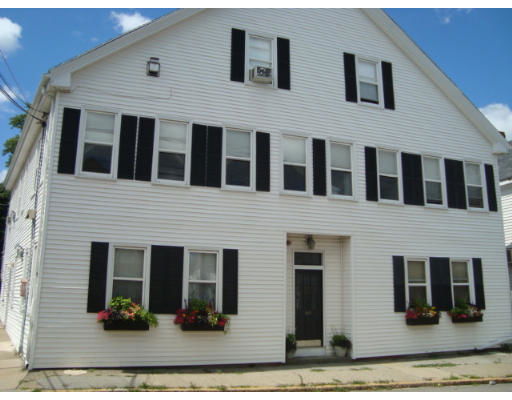 Front view of a multi-story house with white siding and black shutters.