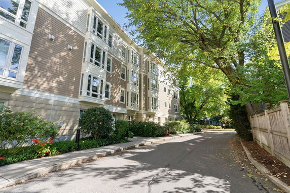Front view of a multi-story residential building with trees and a pathway.