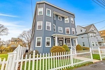 Front view of a tall three-story house with blue siding and a white picket fence.