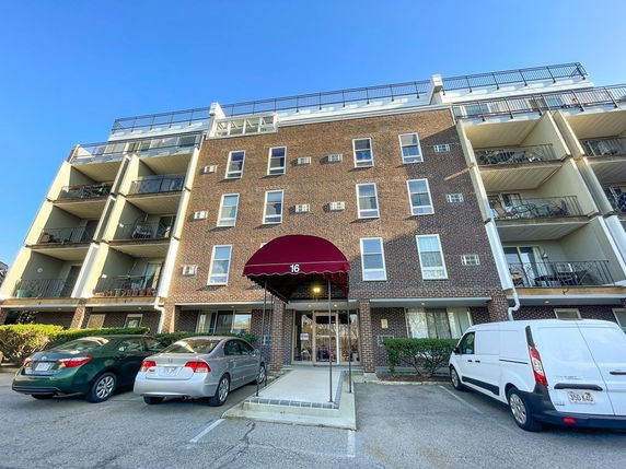Front view of a multi-story brick apartment building with balconies and a red awning.