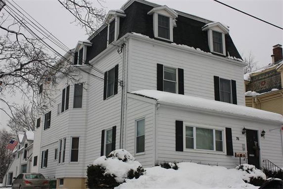 Front view of a multi-story white house with dormer windows and dark roof.