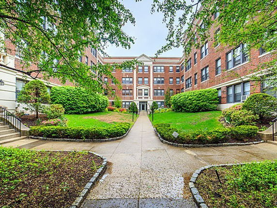 Front view of a multi-story brick building with landscaped gardens and a walkway.