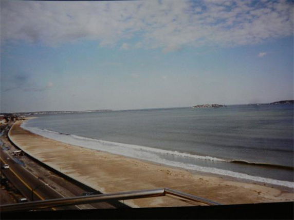 Panoramic view of a beach with waves and a road alongside.