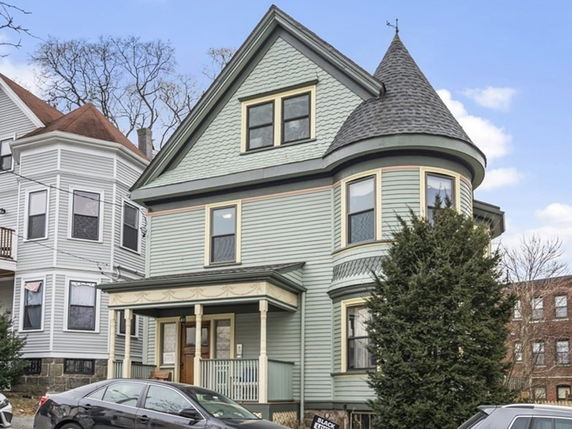 Front view of a three-story house with a turret and porch.