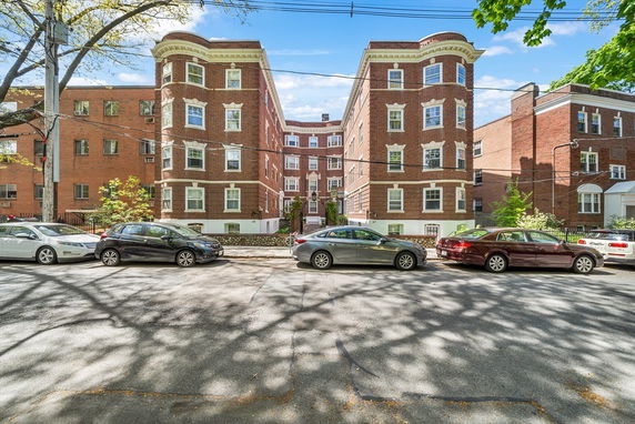Front view of a multi-story brick building with cars parked on the street.