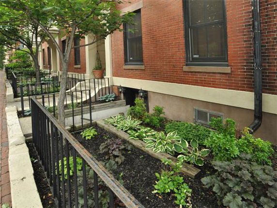 Front view of a brick building with a small garden area and metal fence.