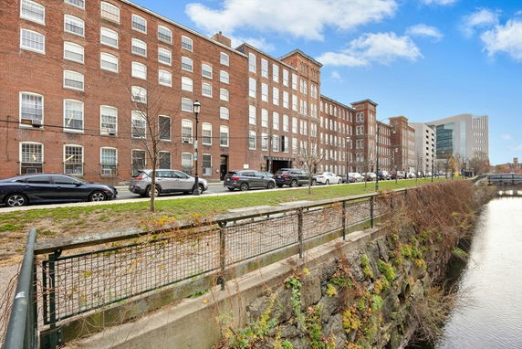 Front view of a multi-story brick building with large windows and a row of parked cars.