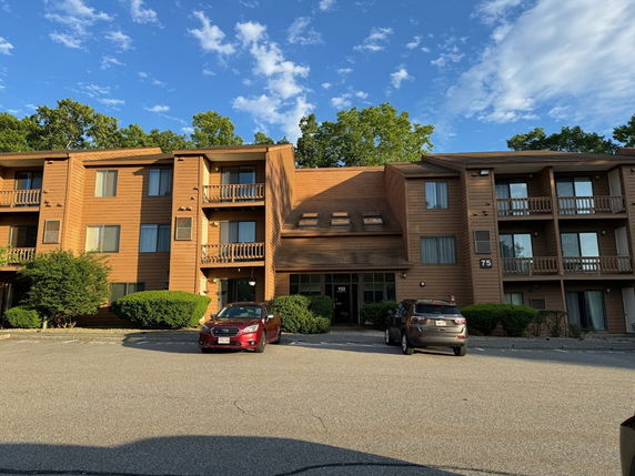 Front view of a three-story apartment building with balconies and a parking area.