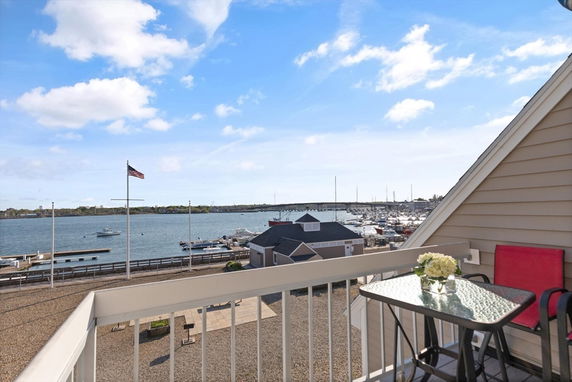 Panoramic view from a rooftop balcony overlooking a waterfront and marina area with boats and a flagpole visible.