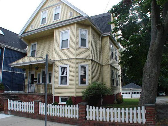 Front view of a multi-story yellow house with white trim and a small front porch.