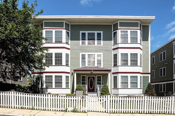 Front view of a multi-story building with distinctive window arrangements and a white picket fence.