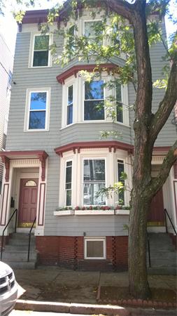 Front view of a multi-story brick house with bay windows.
