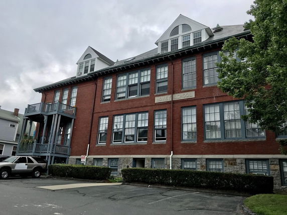 Front view of a multi-story brick building with large windows and a balcony.