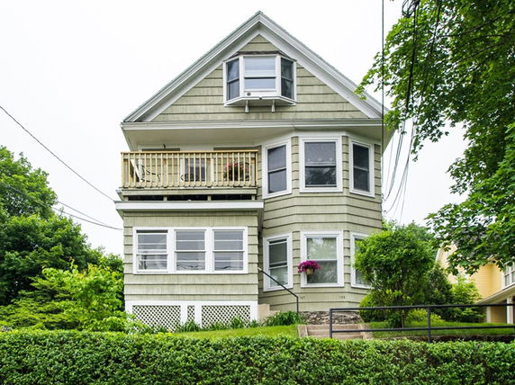 Front view of a multi-story house with a balcony and bay windows.