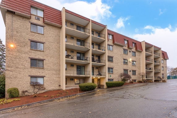 Front view of a multi-story apartment building with balconies and a sloped roof.