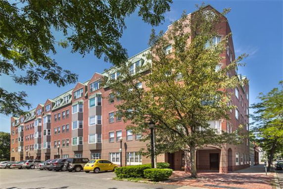 Front view of a multi-story brick apartment building with large windows and a central entrance.
