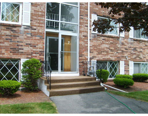 Front view of a multi-story building entrance with brick facade and stairs leading to the door.