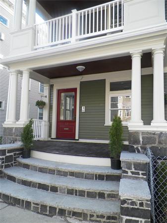 Front view of a house with a red door and stone steps leading up to a porch.