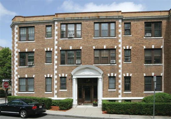 Front view of a brick three-story apartment building with multiple windows and a central entrance.
