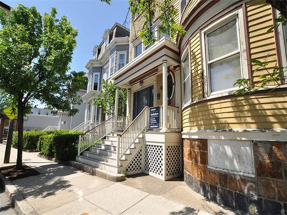 Front view of a multi-story residential building with a porch and stairs.