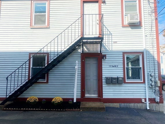 Front view of a building with exterior stairs leading to the second floor and windows with red frames.