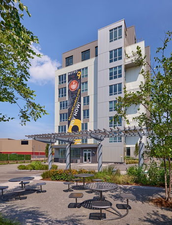 Front view of a multi-story residential building with a pergola and seating area in the foreground.
