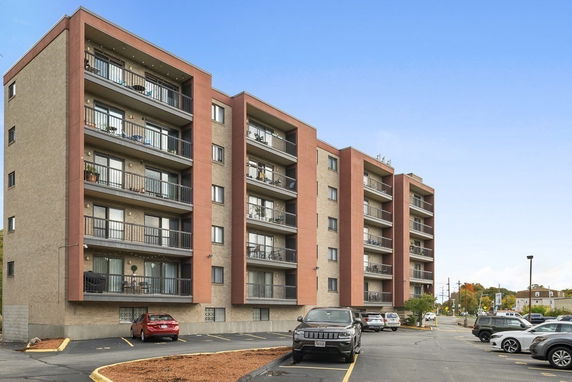 Front view of a multi-story apartment building with balconies and parking area.