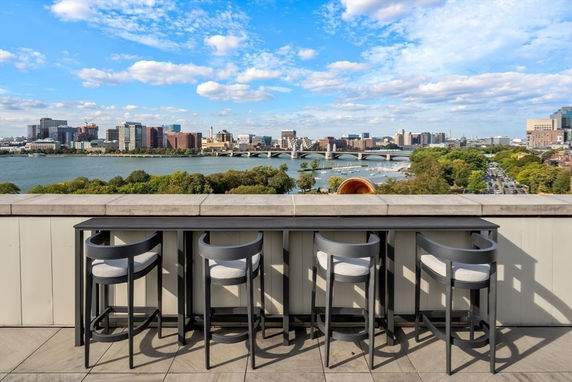 Rooftop seating area with a view of a river and city skyline.