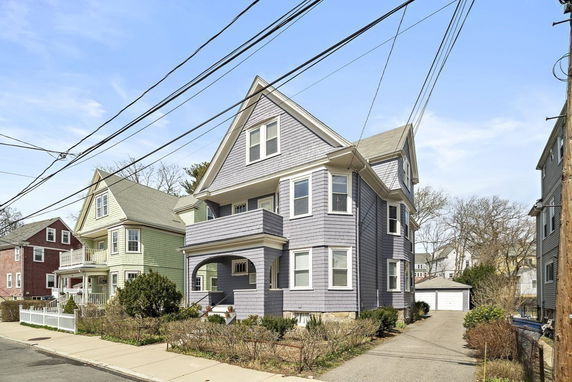 Front view of a multistory house with a gabled roof and a driveway leading to a garage.