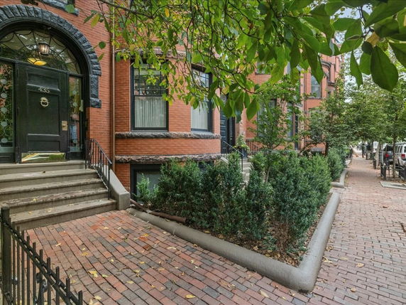 Front view of a multi-story brick townhouse with an arched doorway and steps leading to the entrance.