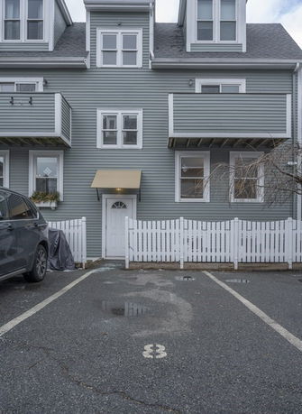 Front view of a multi-story house with a small fenced area and adjacent parking space.