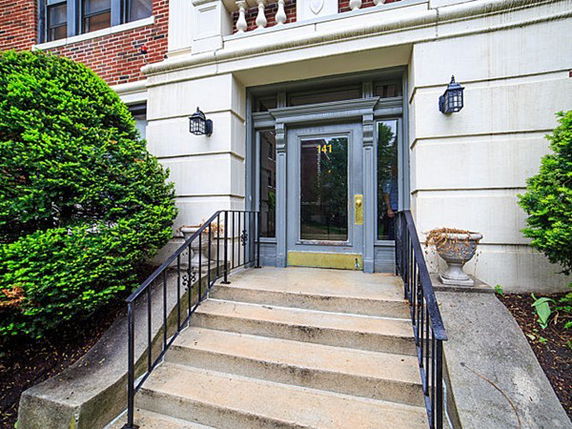 Front entrance of a building with steps leading up to a glass door and surrounding greenery.