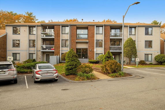 Front view of a three-story apartment building with balconies and parking area.