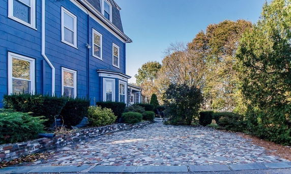 Front view of a blue multi-story house with multiple windows and a cobblestone driveway.