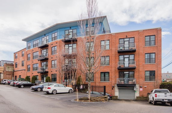 Front view of a multi-story brick building with balconies and a slanted roof.